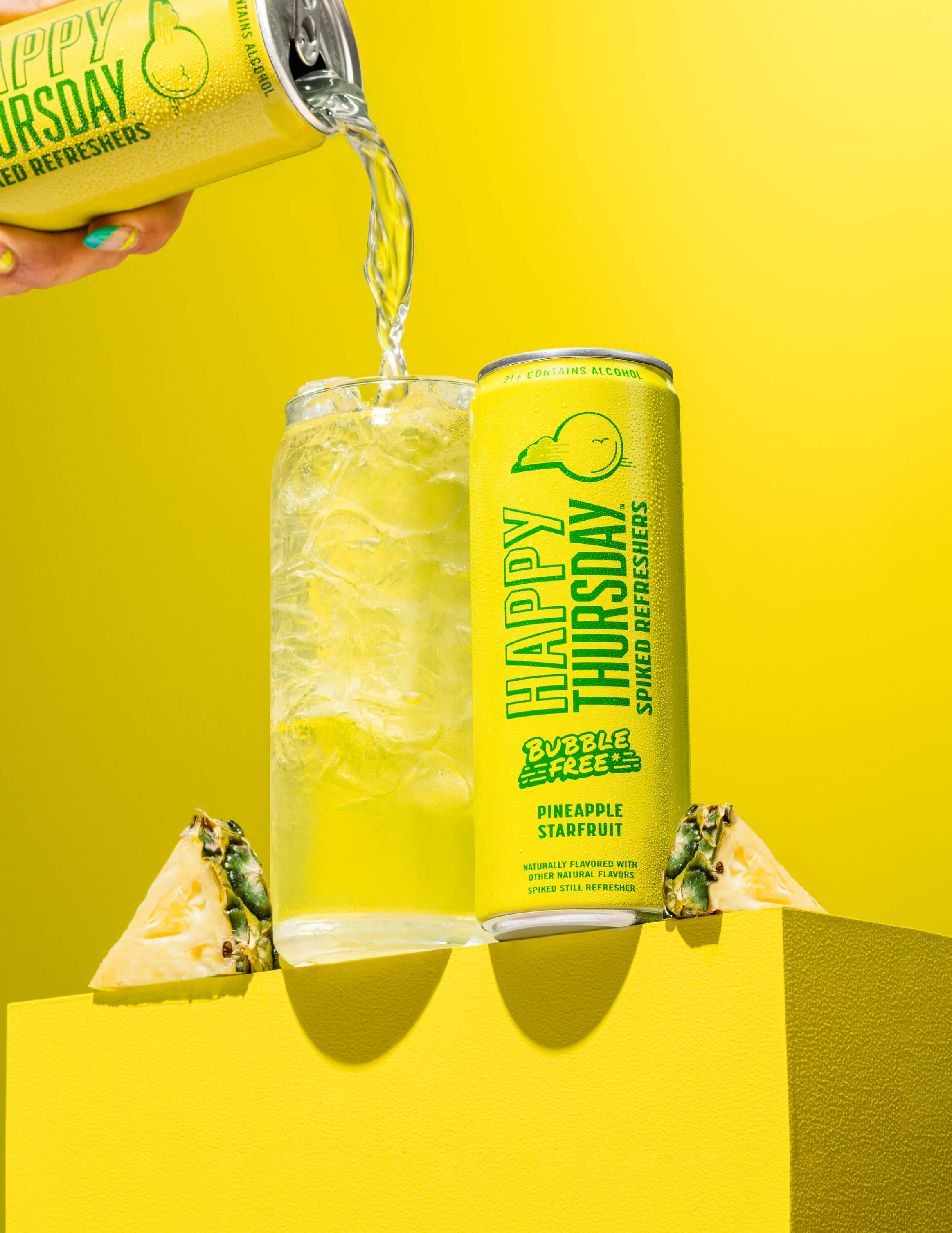 A can of Happy Thursday Pineapple Starfruit Refresher is poured over ice into a glass, with Pineapple Starfruit on a yellow background.