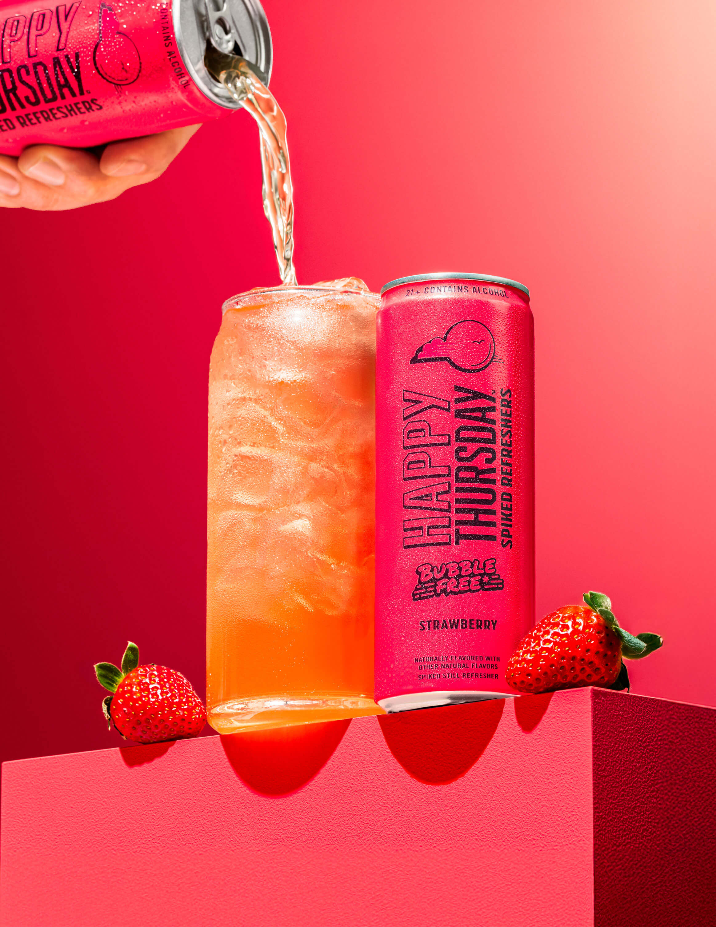 A can of Happy Thursday Strawberry Refresher is poured over ice into a glass, with Strawberry on a pink background.